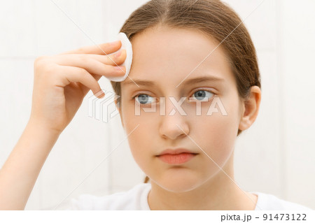 face of a teenage girl, she looks at herself in the mirror and takes care of her skin, does cosmetic procedures using a cotton pad, good and clean skin is a concept of beauty and health 91473122