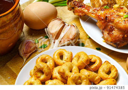 tasty lunch in rural style, healthy food - glass of beer, fried chicken meat and unpeeled potatoes, eggs, green leek, salt and garlic, cooked food on a white wooden boards 91474385