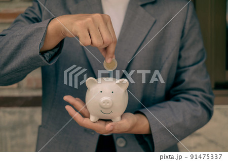 Asian businesswomen hold piggy banks and put coins in piggy banks to save money with coins to step into business, grow successful, and save money. savings concept Asian businesswomen hold piggy banks and put coins in piggy banks to save money with coins to step into business, grow successful, and save money. savings concept 91475337