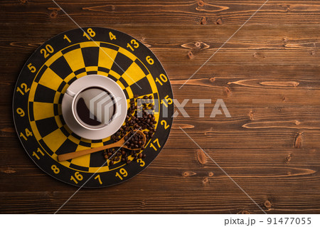 Cup of coffee on dart board on brown wooden table background. Composition with free space for text or design Cup of coffee on dart board on brown wooden table background. Composition with free space for text or design 91477055