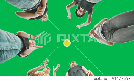 Cheerful schoolgirls play a ball against a green background. 91477653