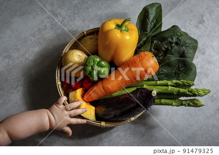 籠に入った野菜の盛り合わせに手をのばす赤ちゃん 籠に入った野菜の盛り合わせに手をのばす赤ちゃん 91479325