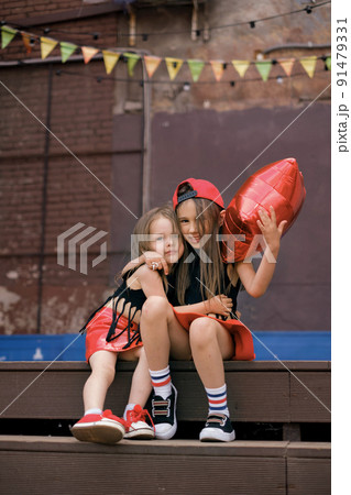 Cute girlfriend girls dressed in hip hop rock hipster style are sitting on the steps of the city street scene cute hugging. Friendship since childhood 91479331