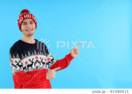 Attractive guy in Christmas sweater on blue background Attractive guy in Christmas sweater on blue background 91480015