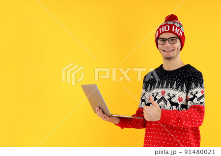 Guy in Christmas sweater with laptop on yellow background Guy in Christmas sweater with laptop on yellow background 91480021