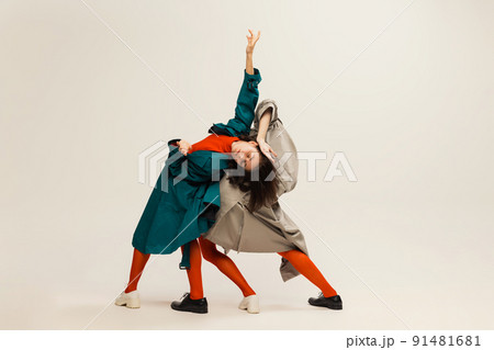 Portrait of stylish man and woman in coats and tights posing isolated over grey studio background. Flexible dance 91481681