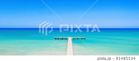 White wooden pier over bright turquoise sea water, panorama of tropical island coast White wooden pier over bright turquoise sea water, panorama of tropical island coast 91485534