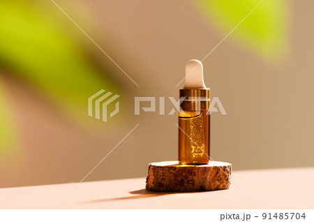 Cosmetic amber glass dropper bottle on wooden podium with oil, serum or fruit peeling in the sunlight. Green ruscus, soft focus. Beauty product presentation, natural background. Front. Mockup concept  91485704
