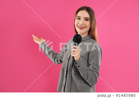 Young female journalist with microphone on pink background 91485980