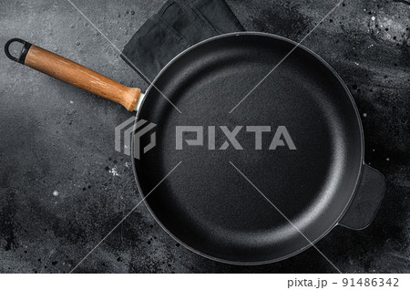 Empty cast-iron skillet for cooking on rustic towel. Black background. Top view. Copy space 91486342