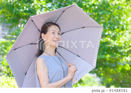 日差しの強い公園で日傘をさして紫外線対策をする笑顔のシニア女性 91488581