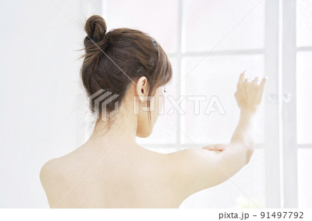 リビングで腕のスキンケアをする女性の後ろ姿 リビングで腕のスキンケアをする女性の後ろ姿 91497792