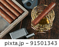 Top view of a Cuban cigar on a glass of whiskey or alcohol. Wooden table, lighter and cutter 91501343