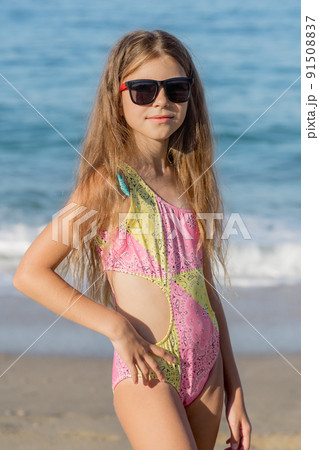 Girl posing on the beach in a pink swimsuit and glasses. 91508837