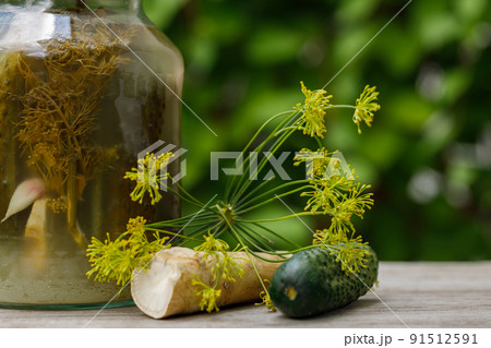Pickles in a jar on an old wooden table in the garden. A summer sunny day. Cucumber, herbs, dill. Background image, copy space, horizontal Pickles in a jar on an old wooden table in the garden. A summer sunny day. Cucumber, herbs, dill. Background image, copy space, horizontal 91512591