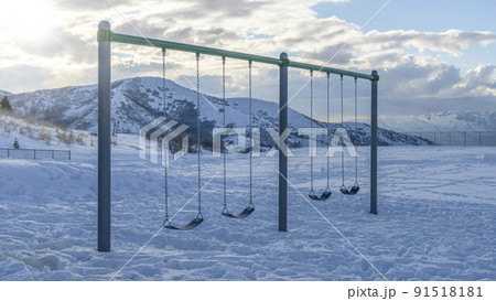 Pano Playground swing with thick snow on ground and views of mountain and cloudy sky Pano Playground swing with thick snow on ground and views of mountain and cloudy sky 91518181