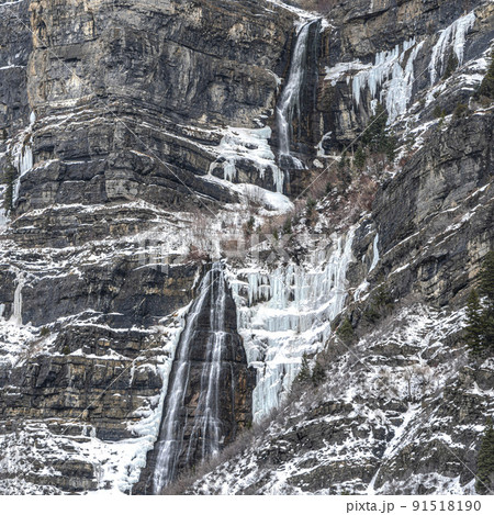 Square frame Snow-covered, rocky mountain side dotted with trees and white snow with falls 91518190