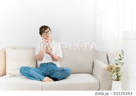 家のソファでスマホを使う女性（困る・悩む） 91520363
