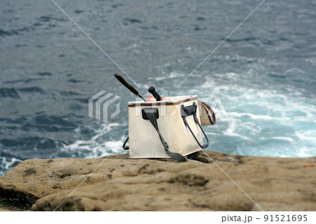サラシの広がる沖磯を背景に白い磯釣り用コマセバッカンのセットを離れた位置から撮った釣り座風景写真 91521695