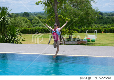 Little girl in a life vest jumps into an outdoor swimming pool. Cute little girl playing in the pool on a sunny day. Summer lifestyle concept. Little girl in a life vest jumps into an outdoor swimming pool. Cute little girl playing in the pool on a sunny day. Summer lifestyle concept. 91522598