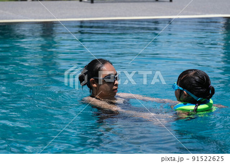 Cute little girl having fun swimming with her mother in the pool on a sunny day. Happy family, mother and her daughter playing in the swimming pool. Summer lifestyle concept. 91522625