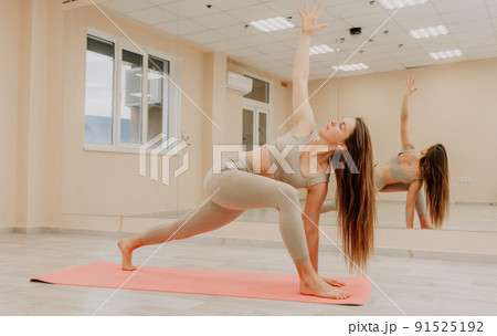 Young sporty woman, fitness instructor in sportswear doing stretching and pilates on yoga mat in the studio with mirror. Female fitness yoga routine concept. Healthy lifestyle and harmony. 91525192