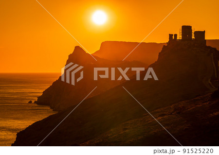 A red burning sunset with the silhouett of a cliff and castle over the sea 91525220