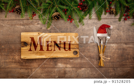 Festive New Year Christmas menu concept. Board with Menu text. Christmas decorations and Cutlery on wooden rustic table. Winter holidays background. Top view, flat lay 91528205