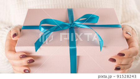 Hands holding pink gift box in package with blue ribbon. Female hands holding Valentine day gift box on white 91528243