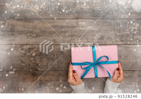 Female hands holding Christmas gift box on rustic wooden background. Xmas and Happy New Year theme, snow, snowflakes. Flat lay, top view 91528246