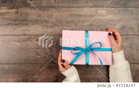 Top view on woman's hands holding Christmas, birthday or Valentine Day celebration gift wrapped in pink paper on rustic wooden background. top view 91528247