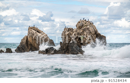 Ocean water splash on rock beach with beautiful sky and clouds. Sea wave splashing on stone at sea shore on winter. Sea waves lash line impact rock on beach Ocean water splash on rock beach with beautiful sky and clouds. Sea wave splashing on stone at sea shore on winter. Sea waves lash line impact rock on beach 91528434