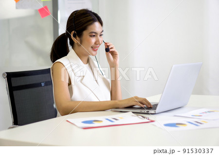 Young asian businesswoman adjusting the headset with mic prepare for online meeting through laptop computer. Working concept social distancing, quarantine, and isolation Young asian businesswoman adjusting the headset with mic prepare for online meeting through laptop computer. Working concept social distancing, quarantine, and isolation 91530337