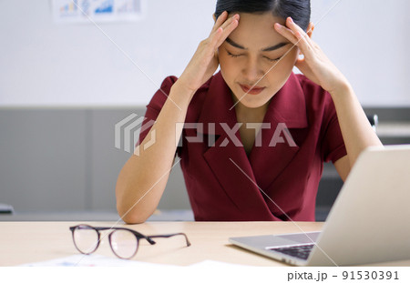 Young asian businesswoman holds her temple with both hands, sitting in the office. The concept of unemployed, sadness, depressed and human problems. 91530391