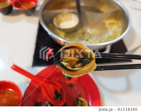 Man uses chopsticks to pick up mussels while eating a hot pot. 91538360