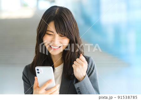 オフィスのエントランスでスマホを見る若いスーツのビジネスウーマン 91538785