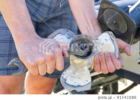 man changing propeller on outboard motor. Repairing outboard motor for boat, replacing screw. 91541086