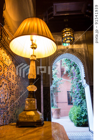 モロッコの街マラケッシュの歴史的なホテル　カラフルなタイル張りの外につながる廊下と脇に置かれたランプ 91541939