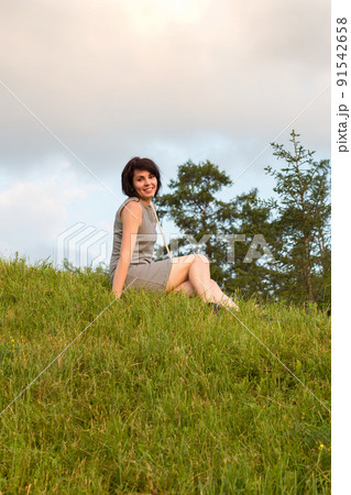 Portrait of a woman in a short dress sitting in a meadow 91542658