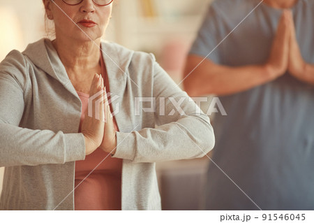 Close-up of calm senior woman in sports shirt holding hands in mudra while achieving mindfulness with meditation at yoga class 91546045