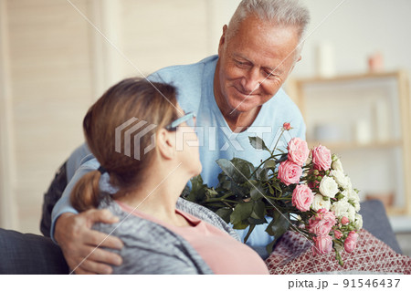 Happy handsome gray-haired man bending to wife and giving beautiful bouquet to her on Valentines day Happy handsome gray-haired man bending to wife and giving beautiful bouquet to her on Valentines day 91546437