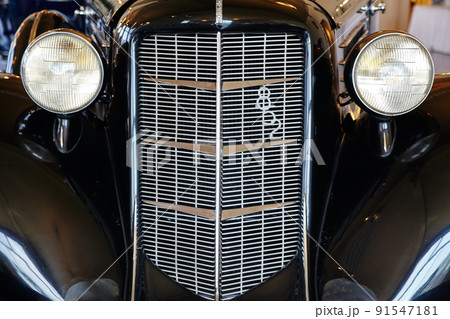 Close-up front shot of an antique car with a tall front grill and two lights like eyes 91547181