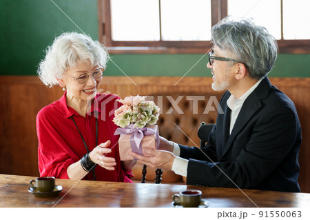 花束とプレゼントを渡す中高年の夫婦 91550063