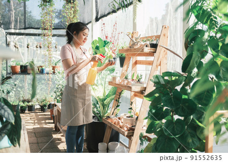 Young woman plant owner shop watering plants in a plant shop. 91552635