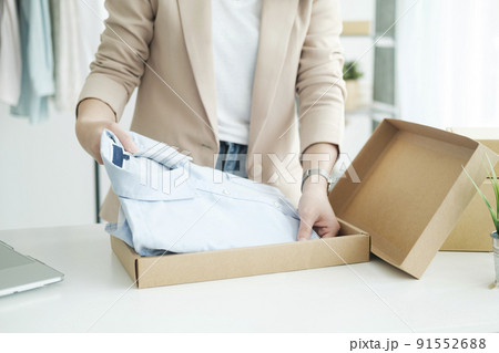 Asian female clothes shop owner folding a t-shirt and packing in a cardboard parcel box. Asian female clothes shop owner folding a t-shirt and packing in a cardboard parcel box. 91552688