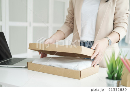 Asian female clothes shop owner folding a t-shirt and packing in a cardboard parcel box. Asian female clothes shop owner folding a t-shirt and packing in a cardboard parcel box. 91552689