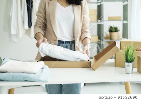 Asian female clothes shop owner folding a t-shirt and packing in a cardboard parcel box. 91552690