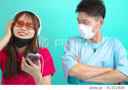 マスクをずらしてヘッドフォンで音楽を聴く女性とそれを睨む男性 91552800