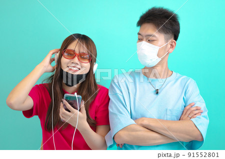 マスクをずらしてヘッドフォンで音楽を聴く女性とそれを睨む男性 91552801