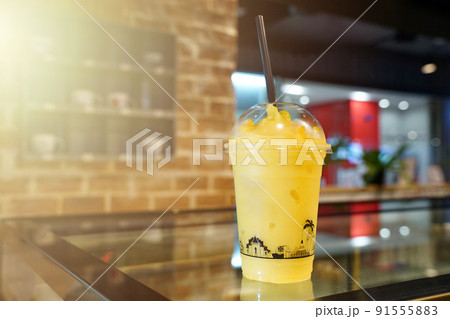 Mango fruity frappe, smoothies and shakes in plastic take away cup on the wooden table in beverage shop. Mango fruity frappe, smoothies and shakes in plastic take away cup on the wooden table in beverage shop. 91555883